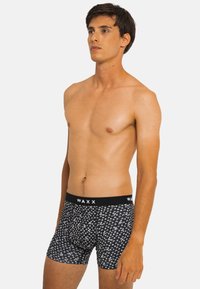 Boxers noirs avec un motif blanc, fabriqués dans un tissu doux. La ceinture arbore le logo "WAXX" en lettres blanches.