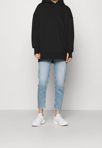 Černá oversized mikina s kapucí, v kombinaci se světle modrými slim džíny a bílými teniskami. Jednoduchý design, měkká textura, volný střih.