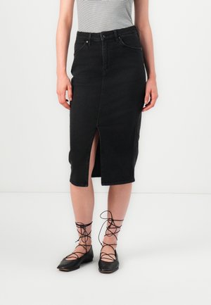 Svart denimskjørt med frontslitt, høy midje og en tettsittende design. Kombinert med svarte snørelaterte flate sko. Stripete topp synlig over skjørtet.