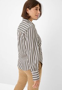 Black and white striped shirt with a collar, long sleeves, and buttoned cuffs; paired with tan pants. Smooth fabric, fitted design.