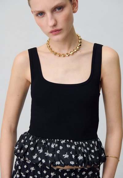 Top senza maniche nero a coste con orlo a peplum a motivo floreale, caratterizzato da una scollatura quadrata. Una collana spessa dorata arricchisce il look.