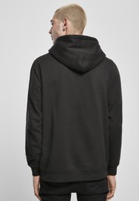 Svart hettegenser med en glatt tekstur, ribbestrikkede mansjetter og nederkant. Har hette med snor og et minimalistisk design uten logoer.