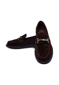 Mocassins en daim marron foncé avec semelles noires et boucles argentées, un chaussure face à l'avant et l'autre de côté sur fond blanc.