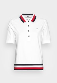 Biała koszulka polo z krótkim rękawem, z czerwono-granatowym paskiem na kołnierzyku, pięcioma czarnymi guzikami i poziomymi paskami na dole. Logo na piersi.