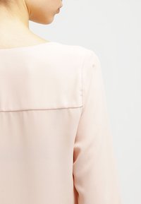 Vaaleanpunainen paita, jossa on sileä tekstuuri. Ominaisuuksiin kuuluu pyöreä kaula-aukko, ja se ulottuu hartioille, esitellen siistiä ja minimalistista muotoilua.