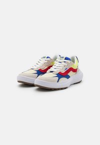 Vans-sneakers med en beige semsket overdel med blå, rød og gul aksenter, en hvit mellomsåle og gummiyttersåle med teksturert grep.