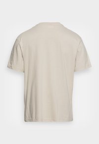 Beżowa koszulka bawełniana z krótkim rękawem pokazana od tyłu, z okrągłym dekoltem i prostymi detalami szycia.