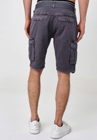 Grå cargoshorts med flera sidofickor, avslappnad passform och fransad nederkant. Bärs med vita sneakers på en neutral bakgrund.