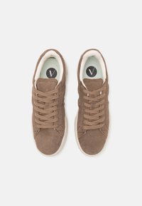 Baskets en suede marron avec lacets plats, une semelle intermédiaire blanche et une semelle intérieure rembourrée vert clair portant un logo noir. Surface texturée.