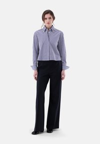 Gestreiftes, kurzes Shirt in Marineblau und Weiß mit langen Ärmeln und Knopfmanschetten, kombiniert mit hoch-taillierten, weit geschnittenen schwarzen Hosen.