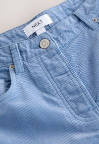 Pantalon en velours côtelé bleu clair avec bouton métallique et étiquette de marque blanche "NEXT" cousue sur la ceinture.