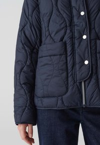 Giubbotto trapuntato blu navy con bottoni a pressione, tasche laterali e chiusura con zip. Presenta un tessuto esterno morbido e testurizzato e una vestibilità comoda.