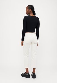 Black ribbed long-sleeve crop top paired with white ankle-length jeans and black platform shoes with studded accents.