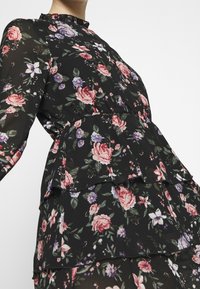 Robe noire à fleurs avec manches longues, col à volants, design en couches, arborant des roses roses et violettes ainsi que des feuilles vertes sur un fond sombre.