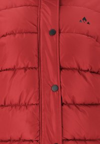 Gilet rembourré rouge fabriqué en tissu lisse, présentant des segments matelassés horizontaux, un col montant et des fermetures à boutons noirs. Petit logo dans le coin supérieur.