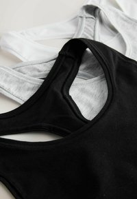 Trei bustiere sportive în negru, gri și alb, realizate dintr-un material moale și elastic, cu design racerback și detalii contrastante la cusături.