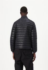 Schwarze Daunenjacke mit gestepptem Design, ausgestattet mit einem Stehkragen und elastischen Bündchen. Glatte, leichte Textur im minimalistischen Stil.