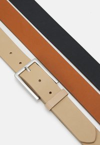 Tres cinturones: uno beige con una hebilla rectangular plateada, uno marrón y uno negro, todos fabricados de cuero liso.