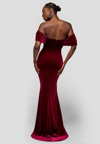 Robe en velours bordeaux avec manches tombantes, silhouette ajustée et longueur jusqu'au sol. Dotée d'une fermeture éclair au dos.