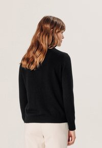 Zwarte wollen trui met een ronde hals, ribgebreide manchetten en zoom. Zachte textuur en aansluitend ontwerp, gedragen over lichtgekleurde broek.