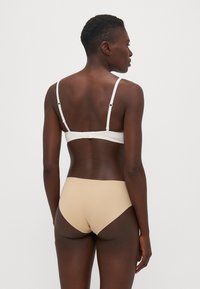 Top bikini bianco con spalline regolabili e chiusura sul retro, abbinato a slip beige a vita alta senza cuciture, che mostrano un tessuto liscio e una vestibilità perfetta.