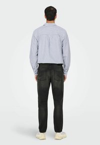 Stribet skjorte i blå og hvid, parret med sorte jeans og lysfarvede sneakers. Har en afslappet pasform og rygdetalje.