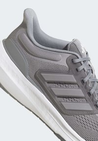 Sneaker sportivo grigio con tomaia in rete, colletto imbottito, suola in gomma e logo a tre strisce Adidas sul lato e sulla linguetta.