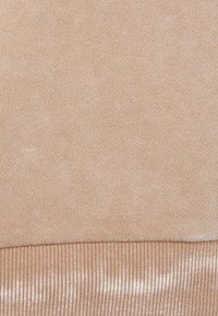 Tejido de un beige claro con una textura suave y de punto. La parte inferior presenta un diseño acanalado, creando un sutil contraste en la superficie.