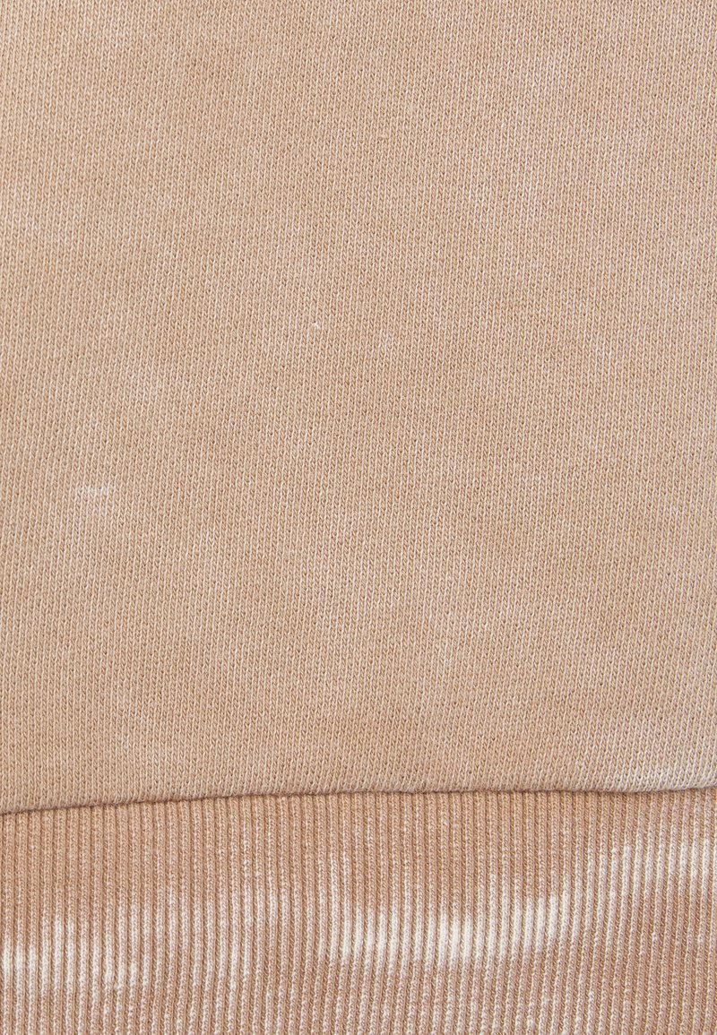 Helles beiges Gewebe mit einer glatten, gestrickten Textur. Der untere Teil weist ein geripptes Design auf, das einen subtilen Kontrast in der Oberfläche schafft.