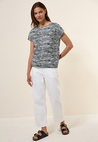 Schwarz-weiß gestreiftes T-Shirt mit kurzen Ärmeln, kombiniert mit weißen weit geschnittenen Hosen und schwarzen Sandalen mit goldenen Akzenten. Glatte Stofftextur.