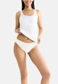 Canotta bianca e biancheria intima color crema con bordo in pizzo. Entrambi i capi presentano un tessuto morbido e un design aderente.