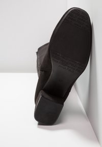 Bottine en daim noir avec un bout carré et un talon bloc robuste. Dotée d'une fermeture éclair latérale et d'une semelle en caoutchouc texturée avec un détail de logo.