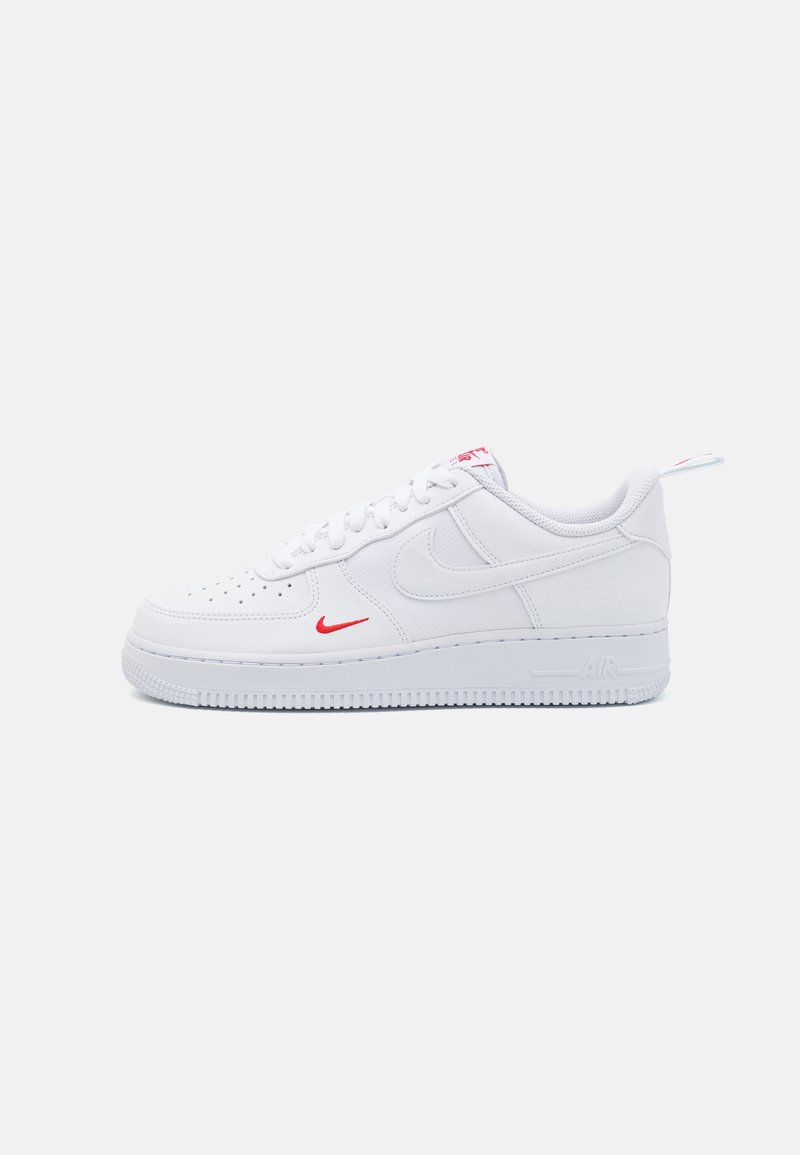 Białe sneakersy Nike Air Force 1 z gładką skórzaną cholewką, czerwoną logo swoosh, białymi sznurówkami, teksturowaną podeszwą środkową i gumową podeszwą.