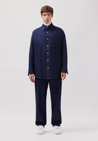 Marineblaue Jeanshemd und passende Hose, mit einer Tasche, Knöpfen und einem bequemen Schnitt. Kombiniert mit weißen Sneakers und einem hochgeschlossenen Oberteil.
