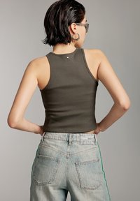 Olijfgroen geribbeld tanktop met een ronde achterkant en een klein logo detail. Gecombineerd met lichtblauwe, hoge taille jeans met groene zijkanten.