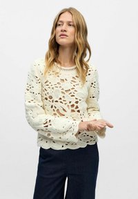 Strikket trøje i creme med blomsterudskæringer og klokkeærmer. Det strukturerede design har åbenstående detaljer over hele tøjet.