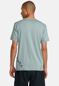 Camisa deportiva de manga corta en color teal con cuello redondo y detalle de logo en el lado izquierdo. Textura suave y tela ligera.