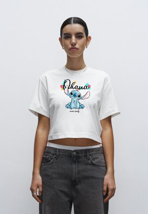 Biały krótki t-shirt z kolorową grafiką Stitche'a oraz napisem "Ohana oznacza rodzinę", zestawiony z szarymi, wysokim stanie jeansami.