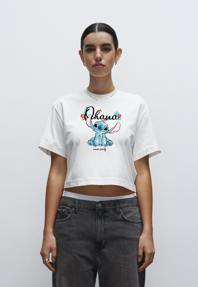 Biały krótki t-shirt z kolorową grafiką Stitche'a oraz napisem "Ohana oznacza rodzinę", zestawiony z szarymi, wysokim stanie jeansami.