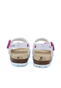 Sandales blanches avec une semelle en liège, présentant des accents roses et des sangles ajustables. Texture lisse avec un détail de design circulaire.