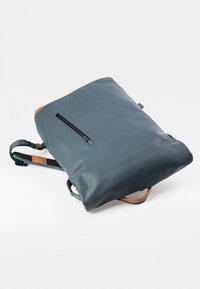Dunkelblauer Leder-Rucksack mit einem hellbraunen Akzent, ausgestattet mit einer einzigen frontalen Reißverschlusstasche und verstellbaren Schulterriemen. Glatte Textur.