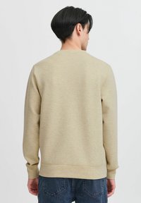 Beige sweatshirt met een subtiele textuur, geribde manchetten en onderkant, ronde halslijn en een ontspannen pasvorm, gedragen met denim jeans.