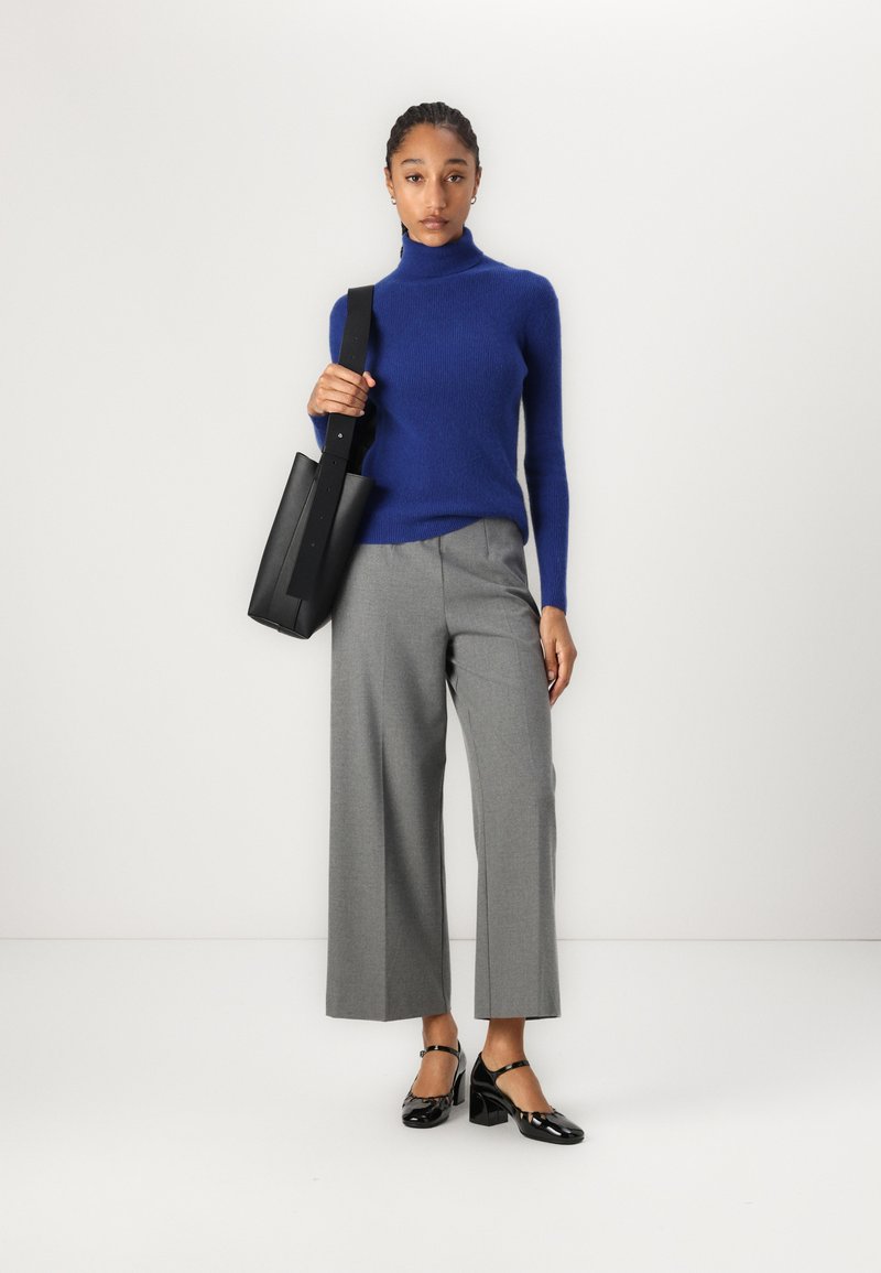 Jersey de lana azul de cuello alto, pantalones de pierna ancha gris claro, bolso de cuero negro y tacones negros de charol con correas en el tobillo.