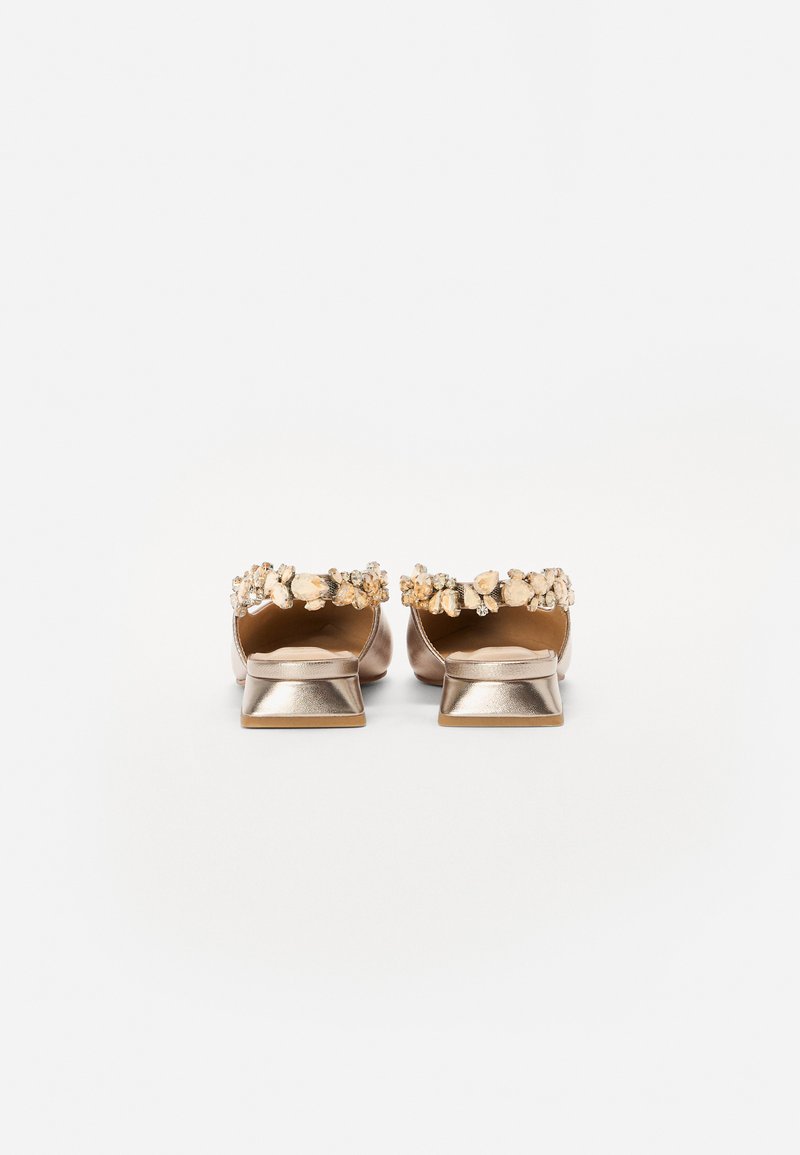 Sandalias de tacón doradas metálicas con tacón cuadrado, adornadas con un grupo de piedras decorativas en el borde superior. Textura suave y parte trasera abierta.