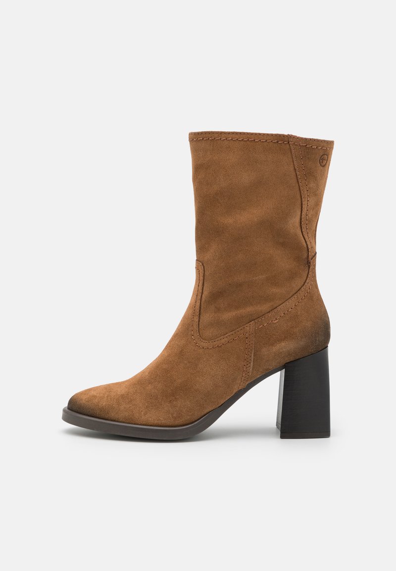 Bottine en cuir suédé brun avec un bout pointu, un détail de couture sur le côté et un talon épais noir. Texture lisse avec une silhouette ajustée.