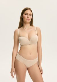 Beżowy biustonosz z wkładkami, z drucikami i regulowanymi ramiączkami, w komplecie z dopasowanymi bezszwowymi majtkami. Gładka tekstura, minimalistyczny design.