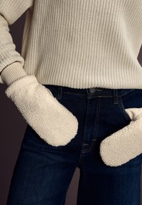 Kremowe, puszyste rękawiczki wykonane z fakturowanej tkaniny, w połączeniu z prążkowanym swetrem i ciemnymi dżinsami, z elastycznym pasem i subtelnym przeszyciem.