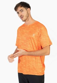 Camiseta atlética naranja con un diseño texturizado y estampado, y cuello redondo. Presenta un logotipo de araña blanca en el lado izquierdo del pecho.