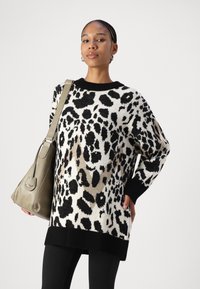 Leopard print sweater in white, black, and beige, with a ribbed black neckline and cuffs. Model holds a gray bag.