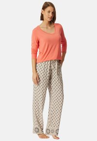 Koraalkleurig long-sleeve top en beige patroon pyjamabroek met zwart geometrisch ontwerp en bloemmotieven bij de boorden. Gemaakt van zachte stof.